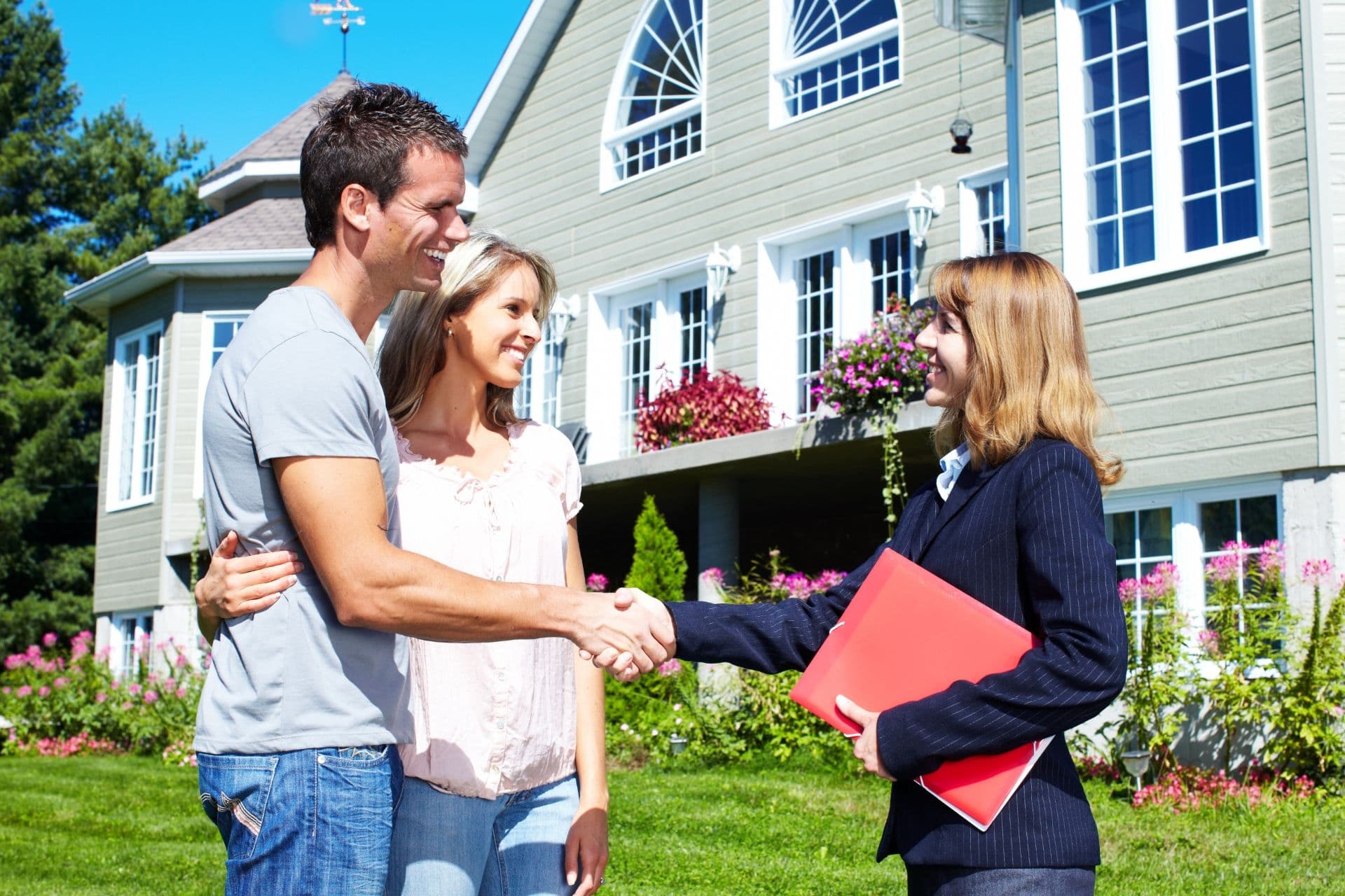 A couple shakes hands with a professional in front of a house.