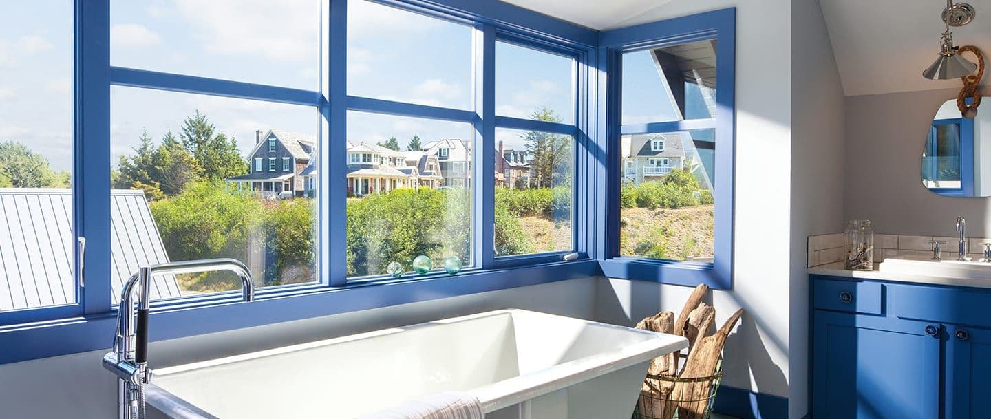 Blue-trimmed vinyl windows in a bathroom with a large white soaking bathtub.